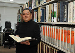 国際文化学部資料室にて。江村教授も制作に携わった手元の『世界の文字大辞典』は古代文字もイラスト化し世界中の文字を歴史的・体系的に解説した一冊