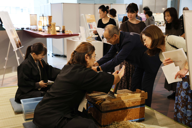 ホワイエで実演された駿河竹千筋細工に見入る来場者ら